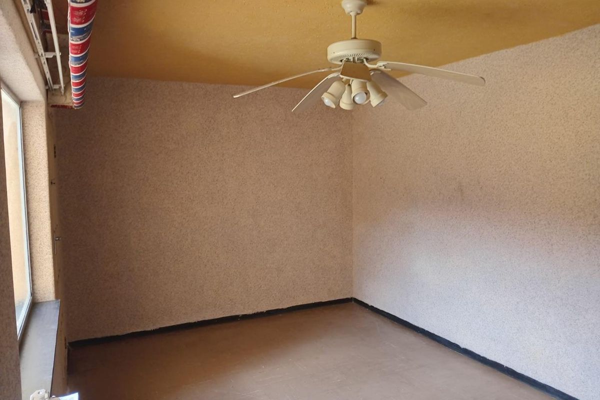 An empty bedroom featuring a ceiling fan, textured walls, and a window, offering a blank canvas for renovation and modernization.