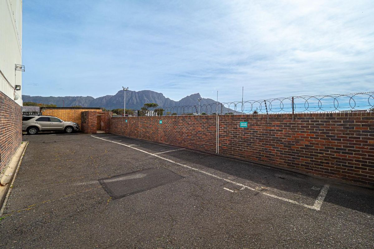 An outdoor parking area featuring a brick boundary wall with security razor wire and mountain views in the background.