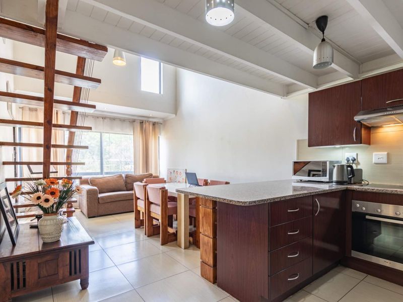 Open-plan living area featuring a modern kitchen with granite countertops, built-in appliances, exposed ceiling beams, and a wooden staircase leading to an upper level.