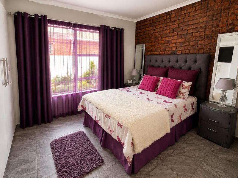 A well-maintained bedroom featuring a prominent exposed brick feature wall, tiled flooring, and a large window with integrated curtain tracks.