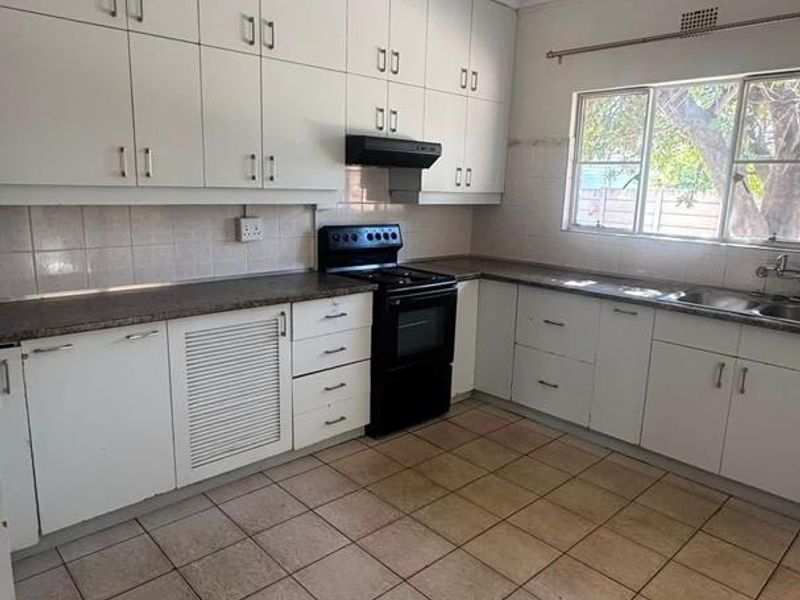 A functional kitchen featuring white built-in cabinetry, laminate countertops, a freestanding stove with extractor fan, and tiled flooring.