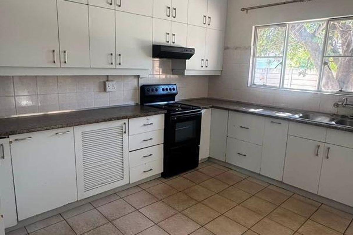 A functional kitchen featuring white built-in cabinetry, laminate countertops, a freestanding stove with extractor fan, and tiled flooring.