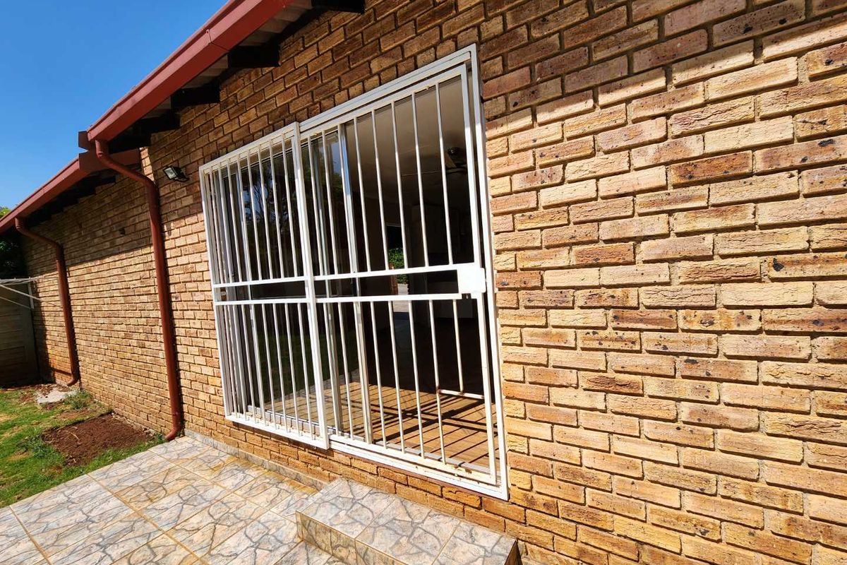 A rear exterior view of the townhouse featuring a face brick facade, a tiled patio area, and a secure sliding door with a metal security gate.