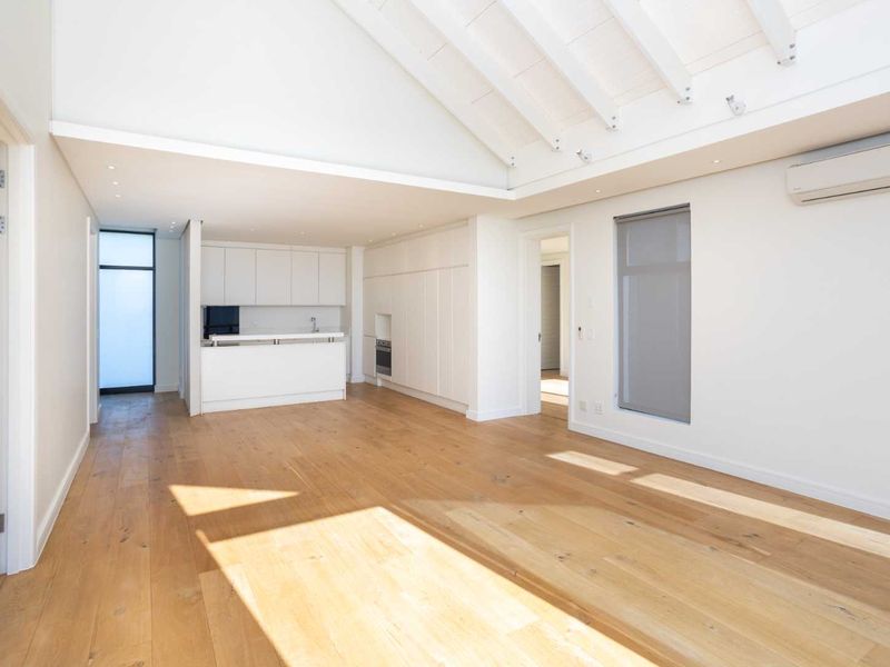 Bright open-plan living area featuring high vaulted ceilings with exposed rafters, timber flooring, and a modern kitchen with integrated cabinetry and appliances.