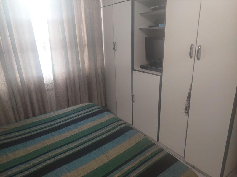 A bedroom featuring built-in cupboards with integrated shelving and a window with curtains.