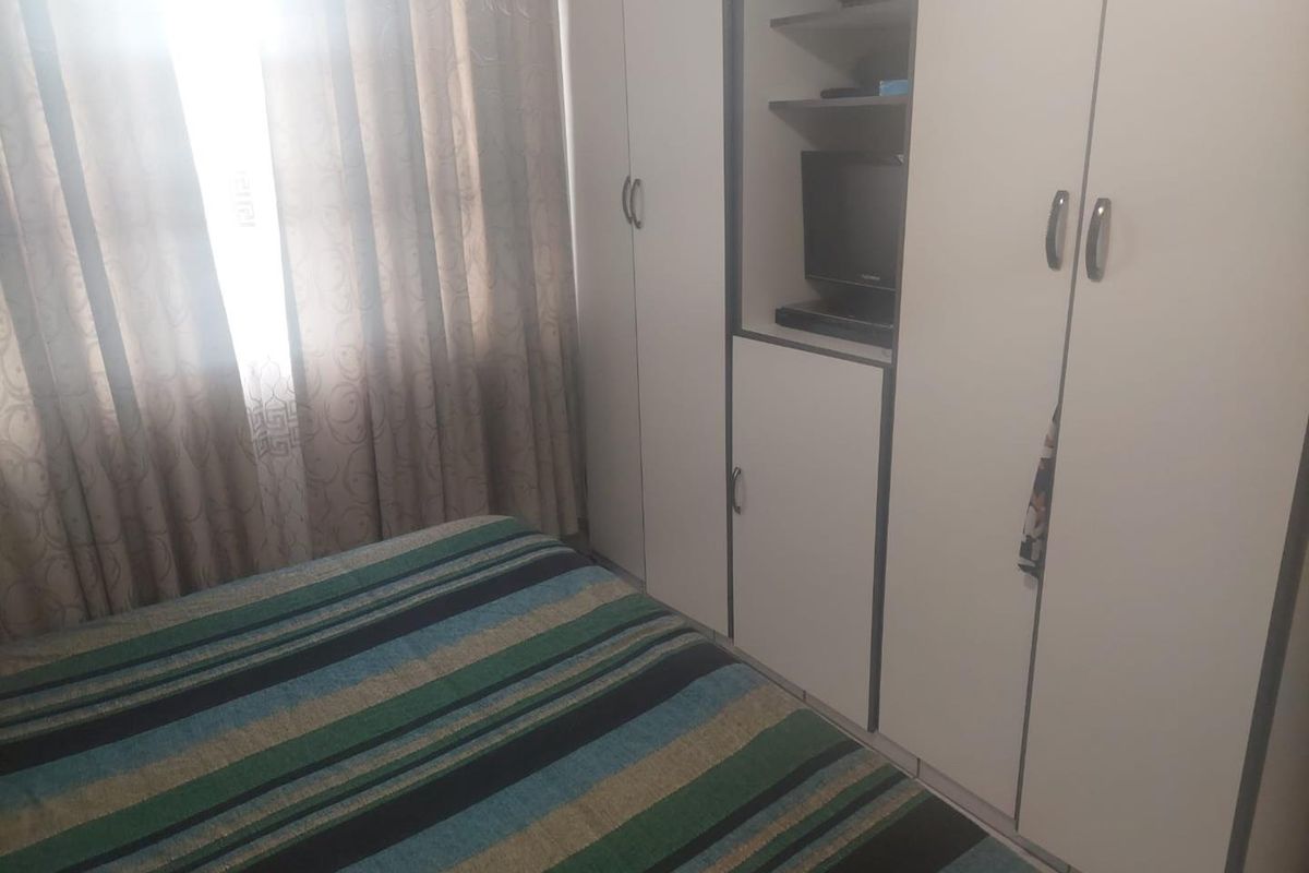 A bedroom featuring built-in cupboards with integrated shelving and a window with curtains.