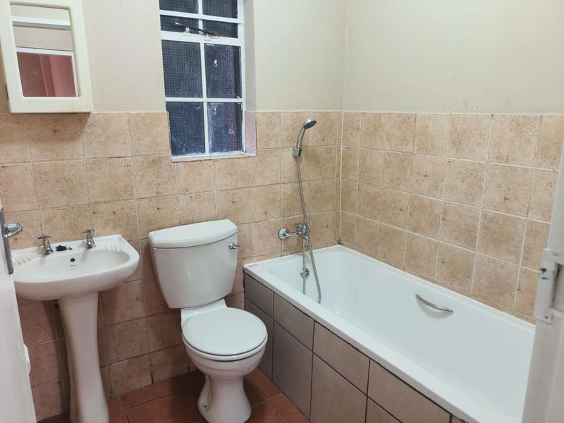 A functional bathroom featuring a pedestal basin, toilet, and bathtub with a handheld shower mixer, finished with tiled walls and flooring.