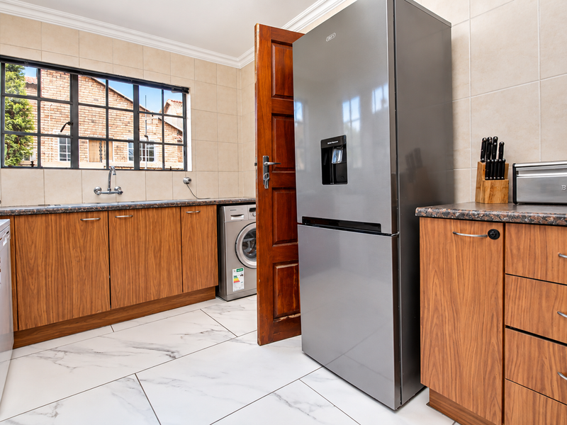 Functional kitchen featuring wood-look cabinetry, marble-effect floor tiles, tiled splashbacks, and integrated laundry plumbing, offering a practical workspace with ample storage.
