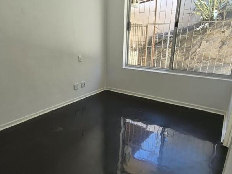 An empty bedroom featuring polished concrete floors, a split-system air conditioner, a ceiling fan, and a window with security bars.