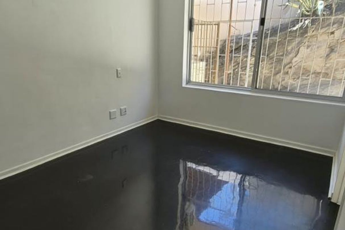 An empty bedroom featuring polished concrete floors, a split-system air conditioner, a ceiling fan, and a window with security bars.