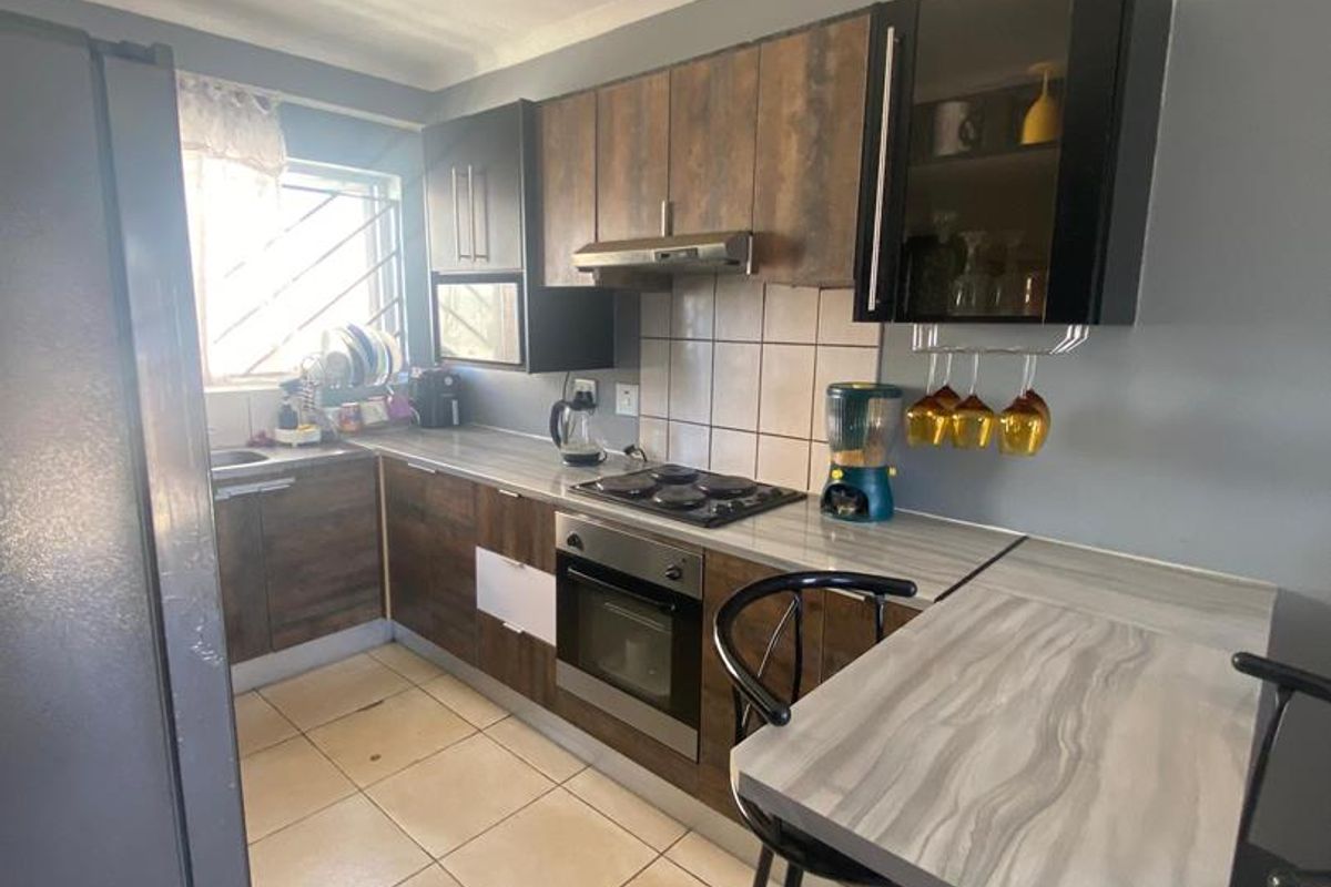Compact kitchen featuring wood-look cabinetry, integrated oven and hob, tiled flooring, and a breakfast bar area.