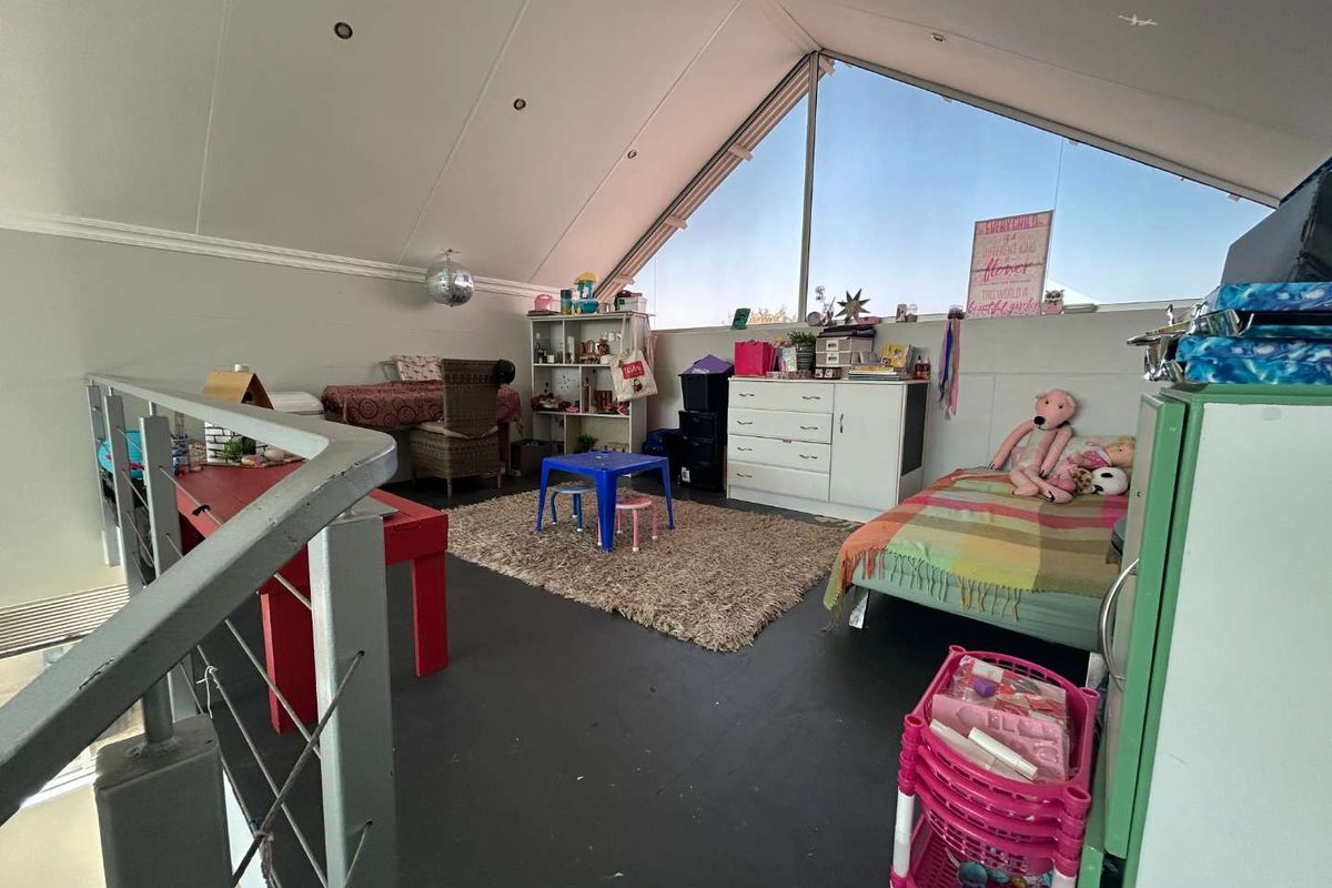 A loft-style bedroom featuring a pitched ceiling, large triangular window, and metal balustrade overlooking the lower level.