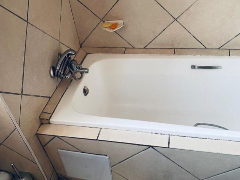 A bathroom featuring a built-in bathtub with wall-mounted fixtures and diamond-patterned ceramic wall tiling.