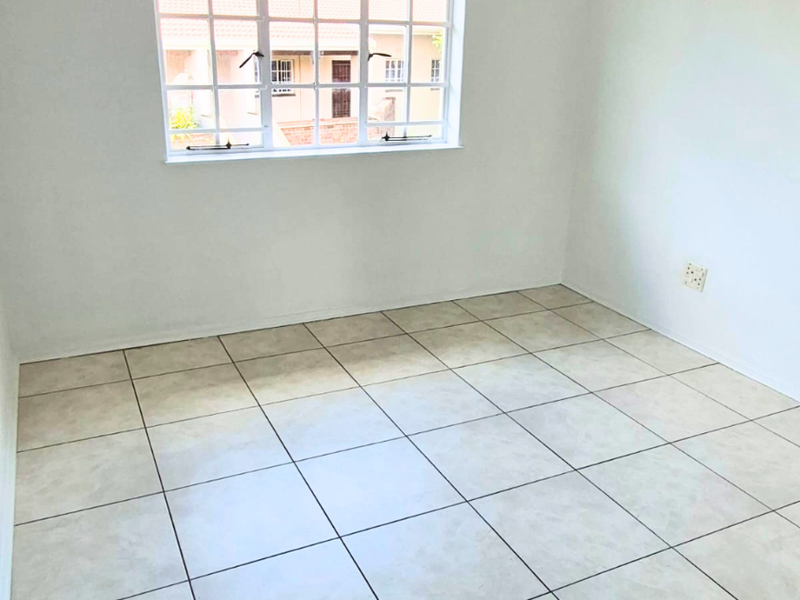 A bright, empty bedroom featuring neutral tiled flooring and a large grid-pattern window, providing a clean canvas for personalization.
