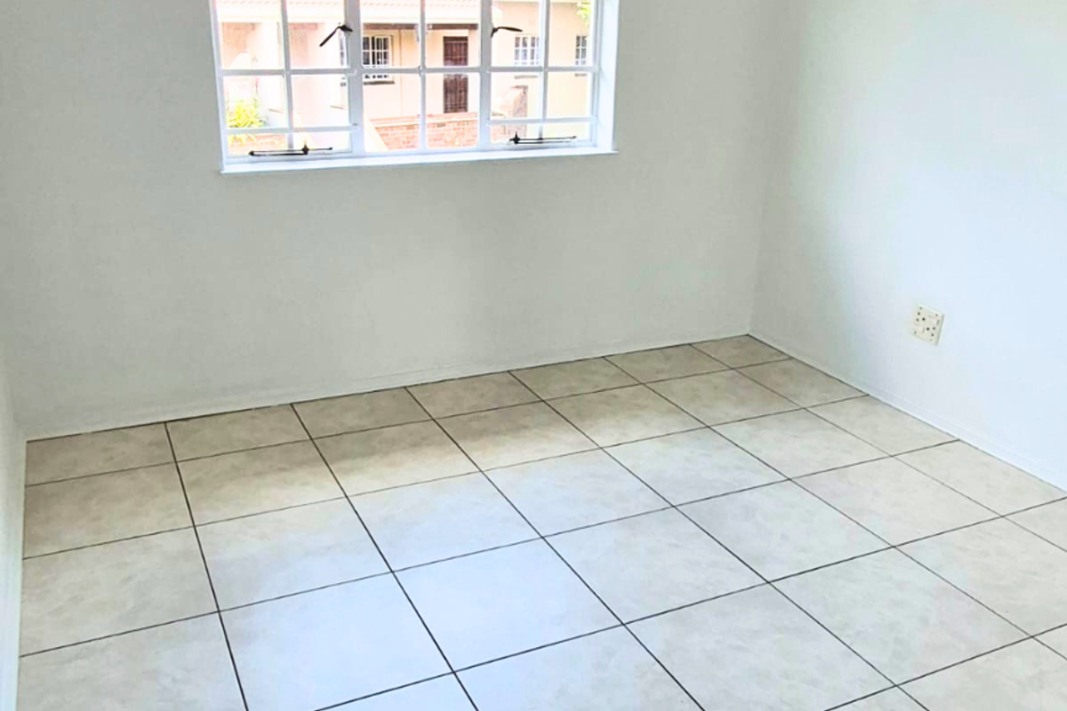 A bright, empty bedroom featuring neutral tiled flooring and a large grid-pattern window, providing a clean canvas for personalization.
