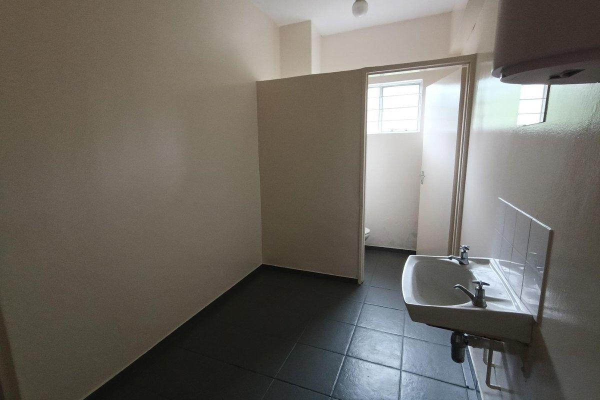 A functional, empty bathroom space featuring a wall-mounted basin, dark tiled flooring, and a partition wall separating the toilet area.