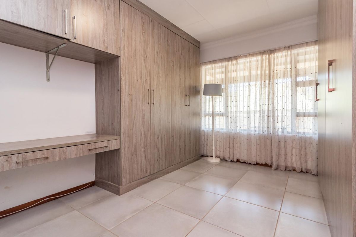 A well-maintained bedroom featuring extensive built-in wooden cabinetry and a dedicated integrated desk area with tiled flooring.