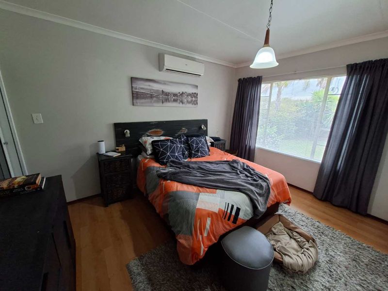 A well-lit bedroom featuring laminate flooring, a wall-mounted air conditioning unit, and large windows with curtain tracks.