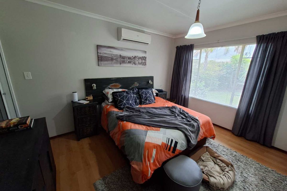 A well-lit bedroom featuring laminate flooring, a wall-mounted air conditioning unit, and large windows with curtain tracks.