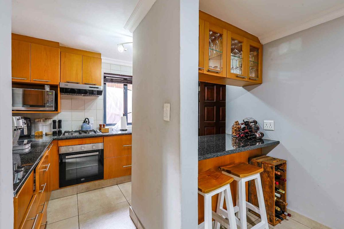 A functional kitchen featuring wooden cabinetry, granite countertops, a built-in oven, and a hob, with an adjacent breakfast bar area.