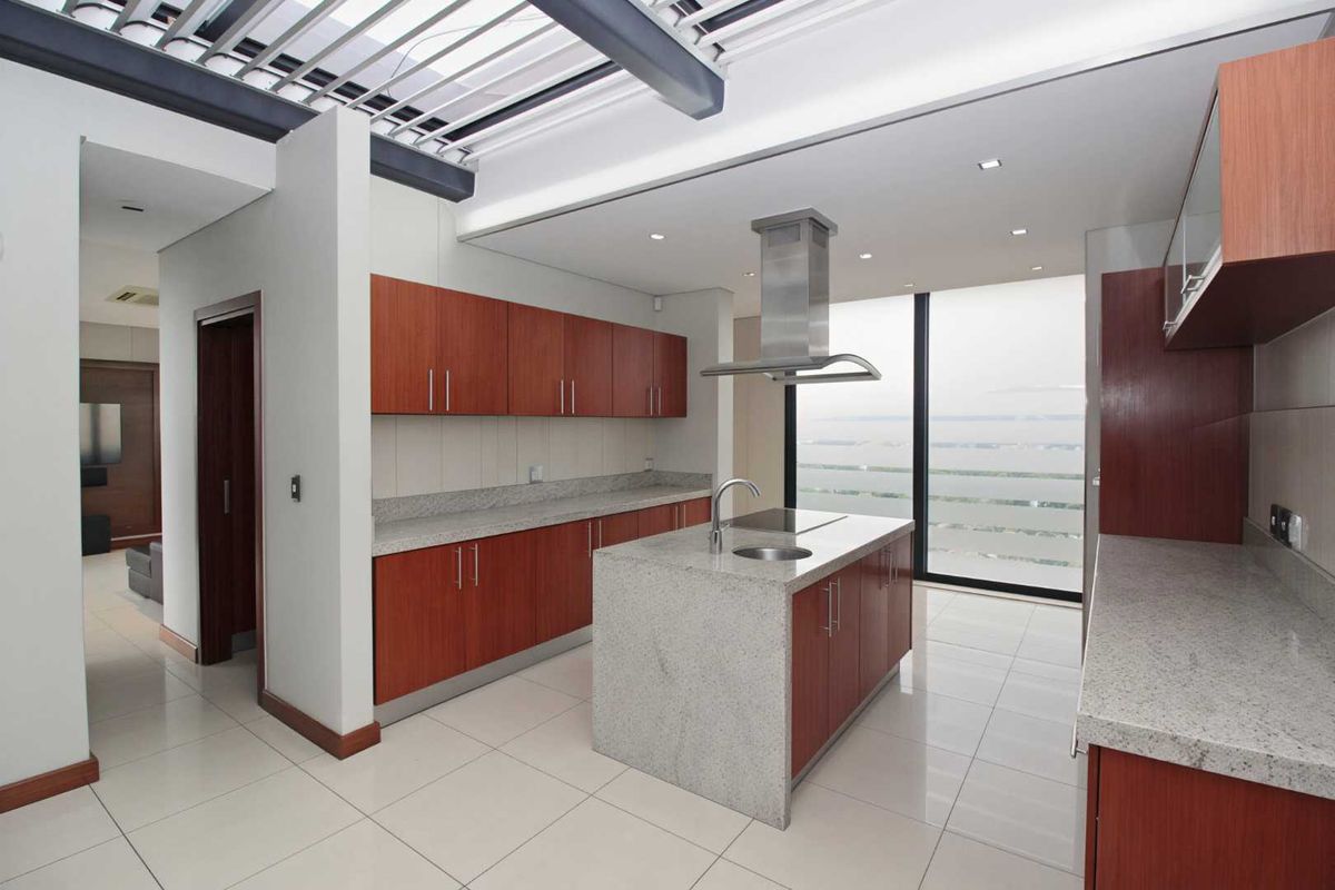 Modern kitchen featuring wood-finish cabinetry, granite countertops, a central island with a built-in cooktop, and a stainless steel extractor fan.