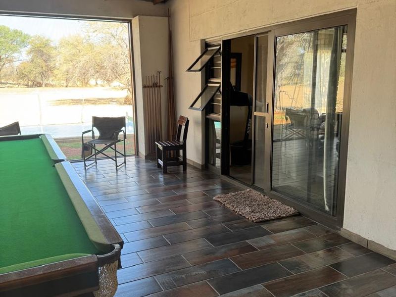 A spacious covered patio featuring exposed timber roof trusses, dark wood-look tiled flooring, and large sliding glass doors leading into the main living area.