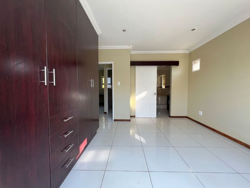 A spacious, empty bedroom featuring large dark wood built-in cupboards, neutral wall tones, and polished white floor tiles with recessed lighting.