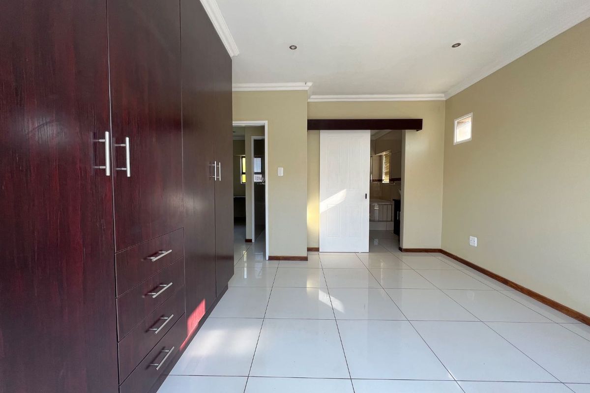 A spacious, empty bedroom featuring large dark wood built-in cupboards, neutral wall tones, and polished white floor tiles with recessed lighting.