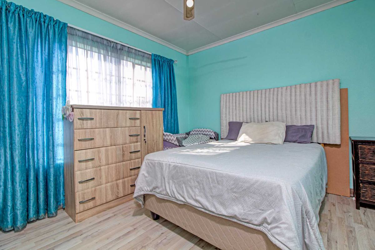 A bedroom featuring light wood-look laminate flooring, a large window with curtains, and a neutral headboard.