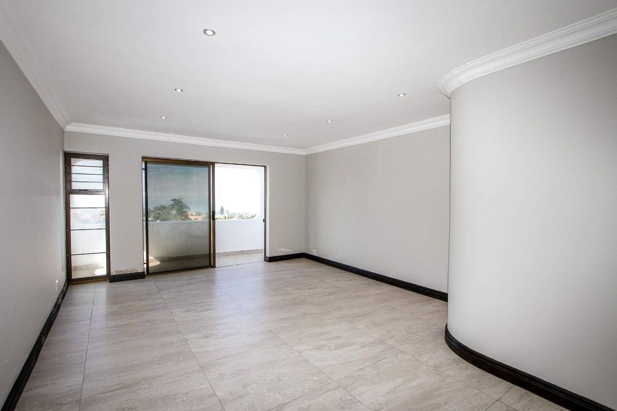 Spacious, light-filled living area featuring neutral tiled flooring, recessed downlighting, decorative crown molding, and sliding glass doors leading to an outdoor balcony.