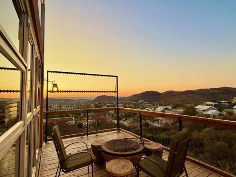 Elevated timber balcony featuring metal railings and expansive glass doors, offering panoramic sunset views over the surrounding landscape.