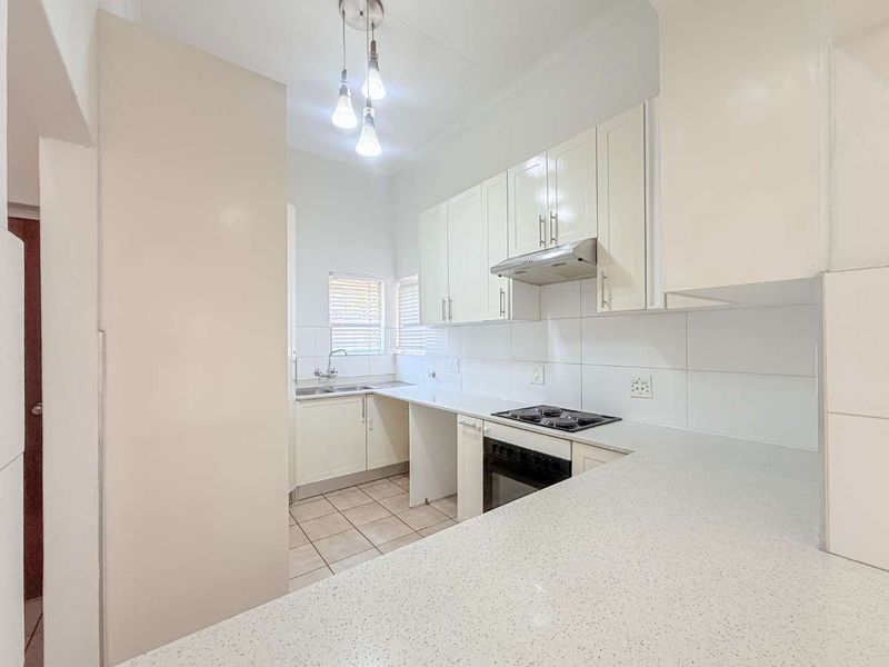 A clean, functional kitchen featuring white cabinetry, stone countertops, built-in oven and hob, and tiled finishes, offering a bright and practical workspace.