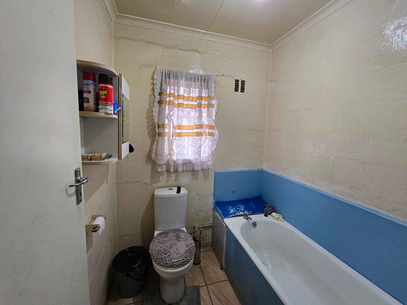 A dated bathroom featuring a bathtub, toilet, and tiled flooring, currently in need of cosmetic updates and wall refinishing.