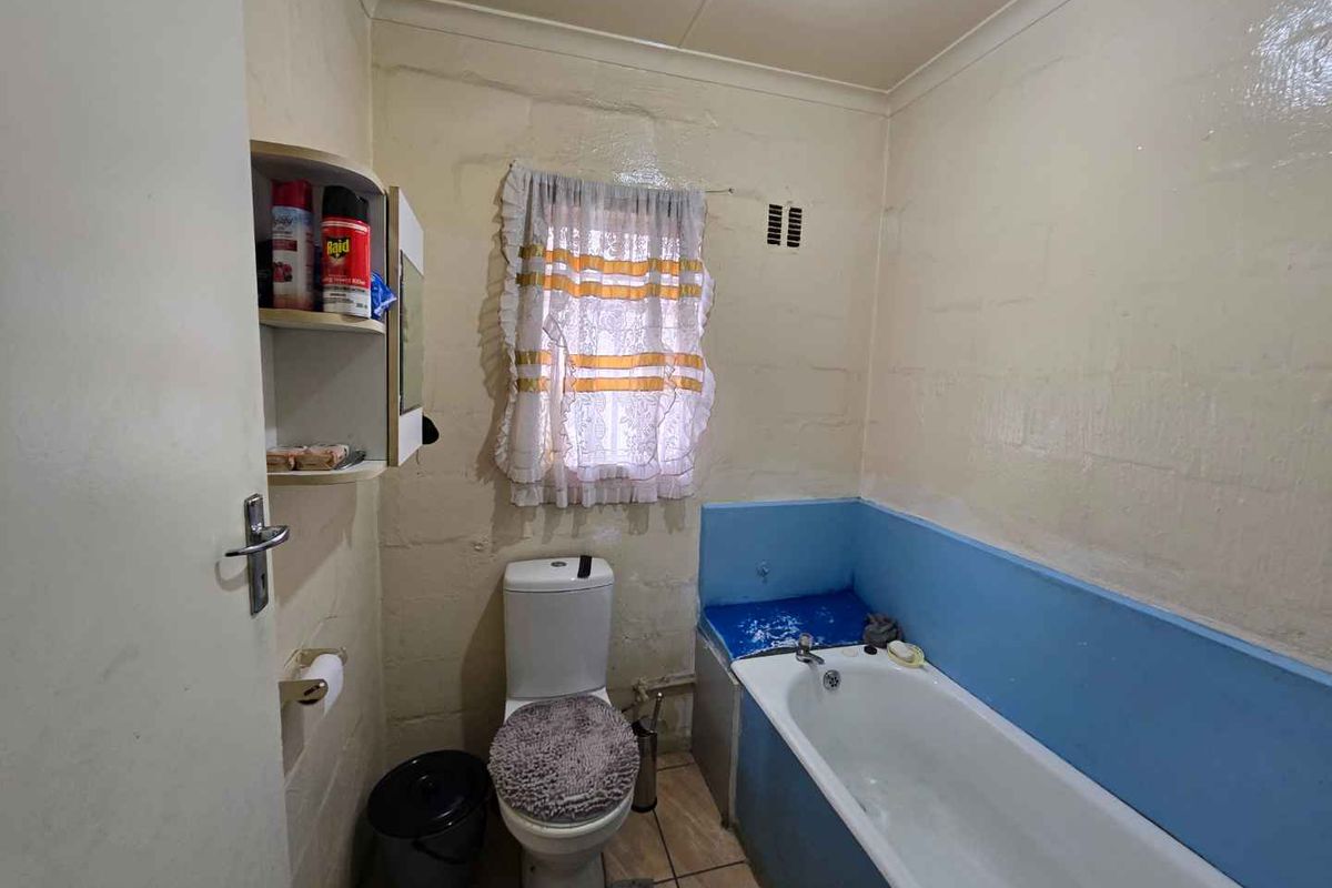 A dated bathroom featuring a bathtub, toilet, and tiled flooring, currently in need of cosmetic updates and wall refinishing.