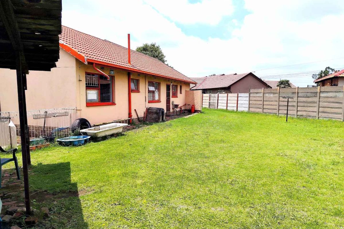 Rear view of the house featuring a tiled roof, exterior wall finishes, and a spacious backyard with a perimeter boundary wall.