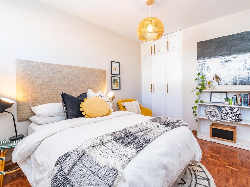 A well-maintained bedroom featuring classic parquet flooring, a built-in wardrobe with modern hardware, and a stylish pendant light fixture.