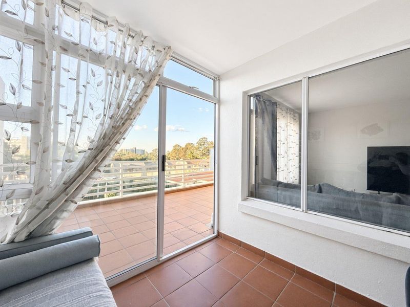 A bright, enclosed balcony featuring tiled flooring, large sliding glass doors, and expansive windows offering an elevated view of the surrounding area.