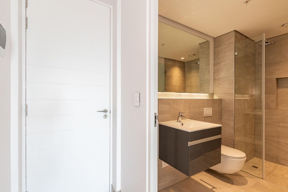 Modern bathroom featuring a wall-mounted vanity, glass shower enclosure, wall-mounted toilet, and neutral floor-to-ceiling tiling with recessed lighting.