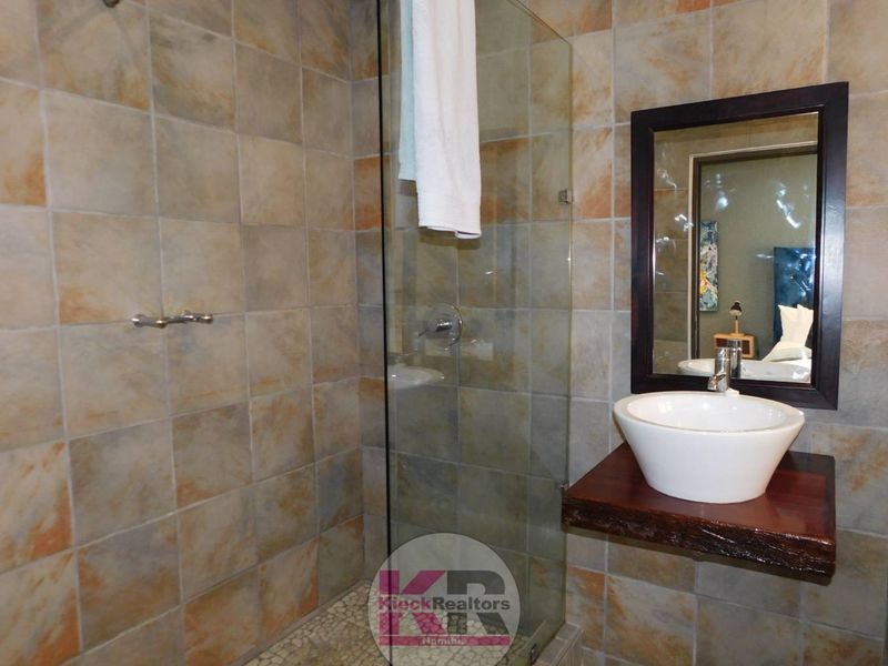 Modern bathroom featuring a glass-enclosed shower with pebble flooring, a vessel sink mounted on a rustic wooden shelf, and tiled wall finishes.