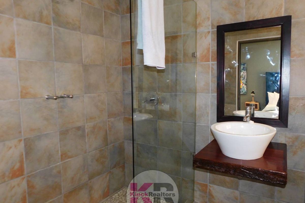Modern bathroom featuring a glass-enclosed shower with pebble flooring, a vessel sink mounted on a rustic wooden shelf, and tiled wall finishes.