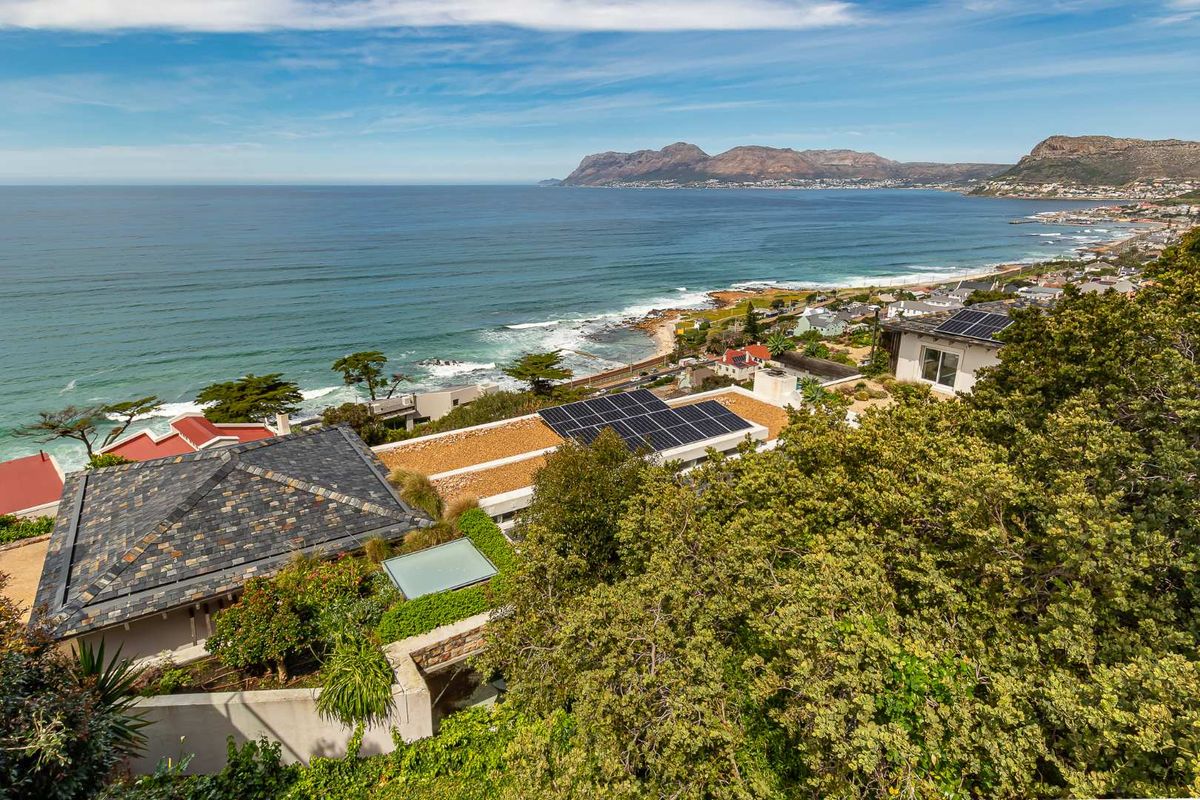 Elevated aerial view showcasing the property's coastal location, featuring solar panel installations on the roof and expansive ocean and mountain vistas.