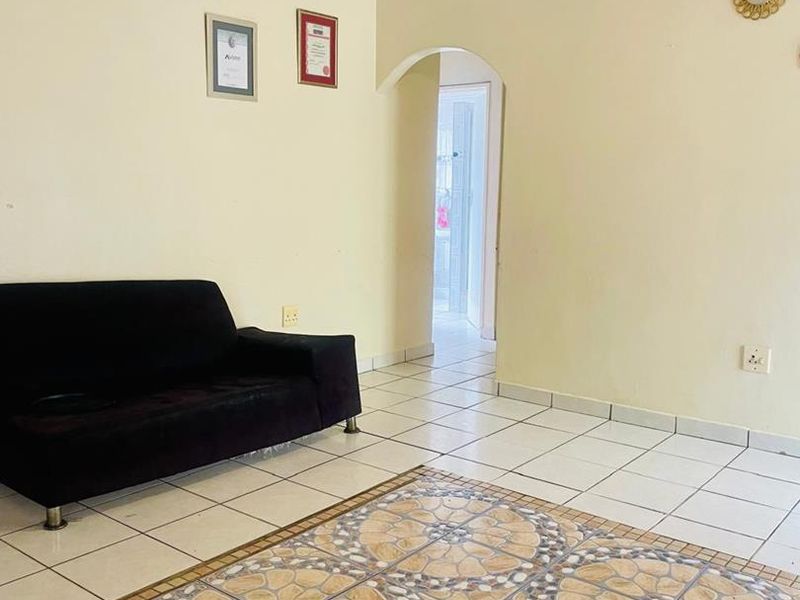 A living room area featuring ceramic tiled flooring, a ceiling fan, and an arched doorway leading to an adjacent space.