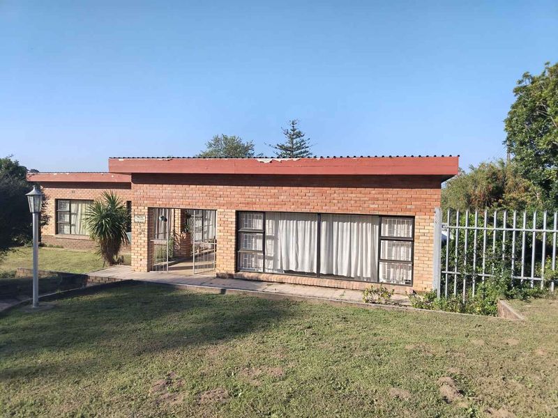 Front elevation of a single-story face brick house featuring steel window frames, security bars, and a flat roof design set on a grassed lot.