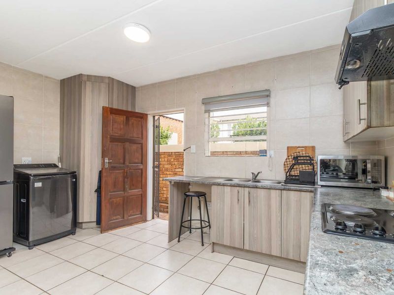 Functional kitchen featuring wood-look cabinetry, laminate countertops, tiled finishes, and direct access to an exterior area through a secure door.