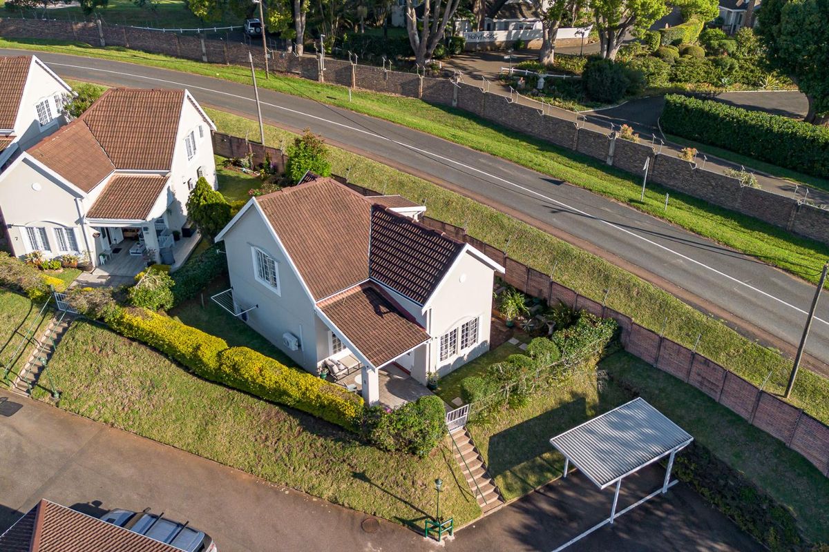 Aerial view of a townhouse property featuring a tiled roof, covered patio, landscaped garden, and a dedicated carport.