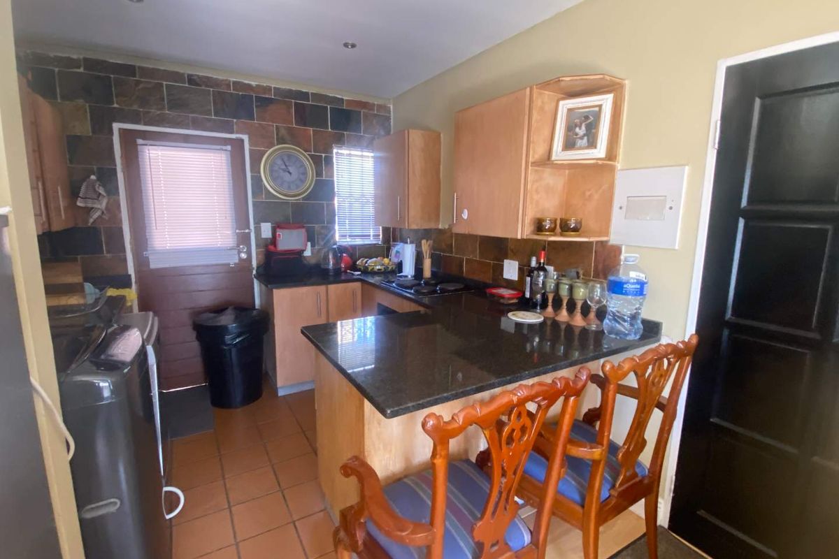 A functional kitchen featuring dark granite countertops, wooden cabinetry, a tiled backsplash, and a breakfast bar area.