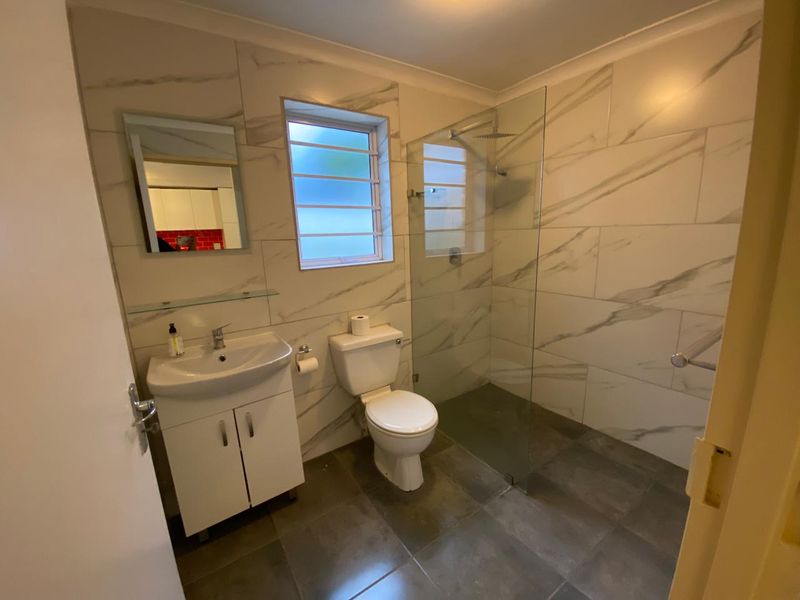 Modern bathroom featuring marble-look wall tiles, a glass walk-in shower with rain head, vanity basin, and louver window for natural ventilation.