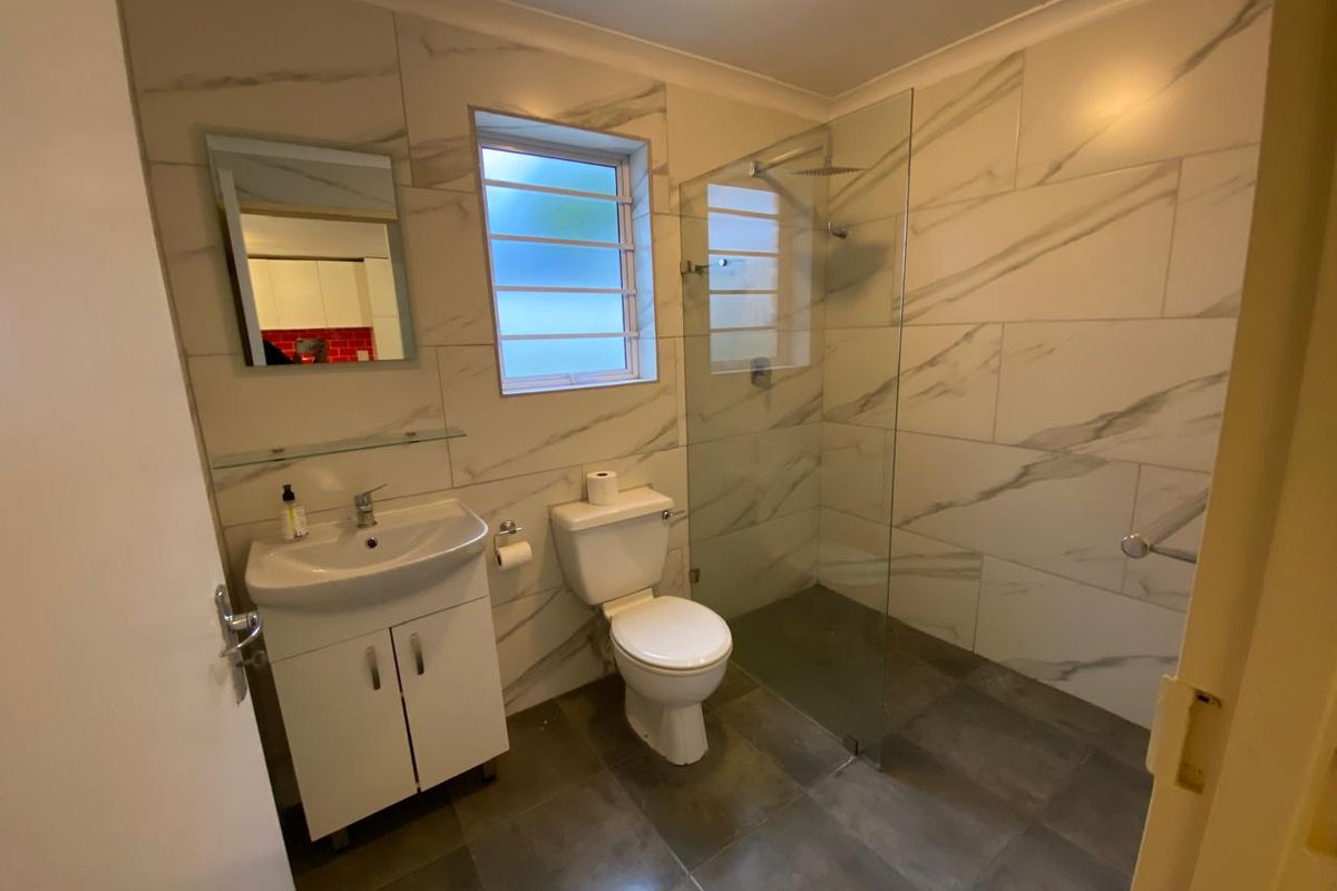 Modern bathroom featuring marble-look wall tiles, a glass walk-in shower with rain head, vanity basin, and louver window for natural ventilation.
