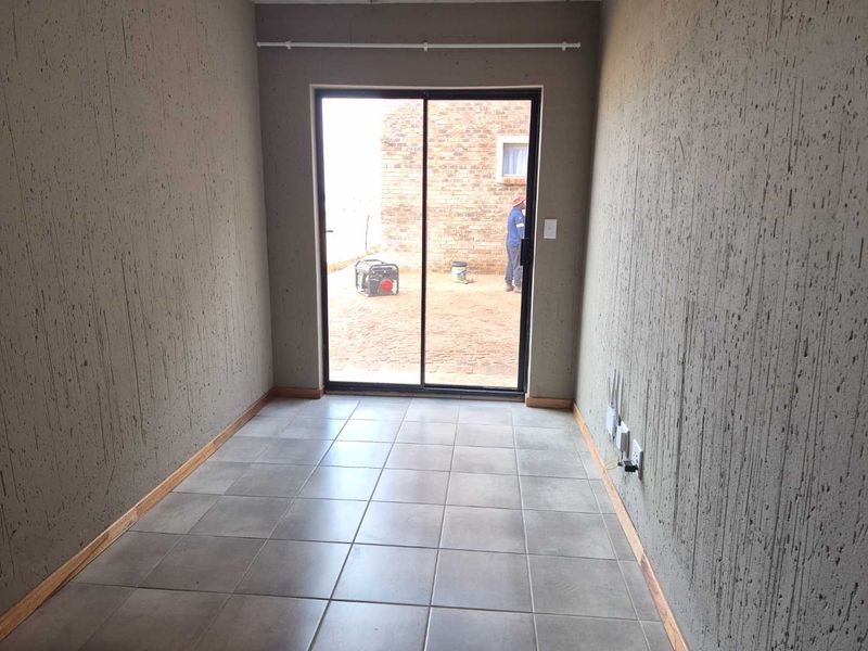 An empty living area featuring textured walls, ceramic floor tiles, and a sliding glass door providing access to the exterior.