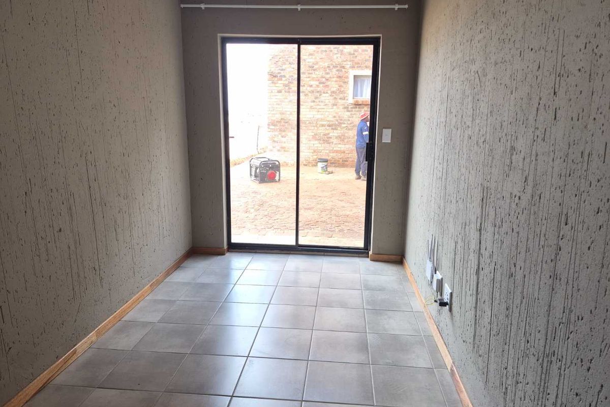 An empty living area featuring textured walls, ceramic floor tiles, and a sliding glass door providing access to the exterior.